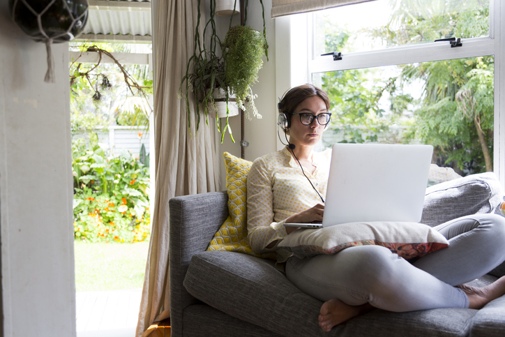 Woman working from home sitting on a sofa working on a laptop wearing a headset