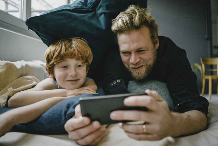 Portrait of father and son lying on couch looking at cell phone